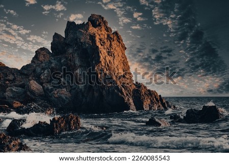 Sunset on the beach with a huge rock and sea waves. Stunning colourful clouds with their magnificent shadows, the shadow of the sun on the big rock