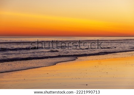 

Sunset on beach with reflections of the orange sky in the water 