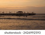 Sunset on Huanchaco beach, Trujillo, Peru, overlooking the old pier, with the sea, waves and surfers.