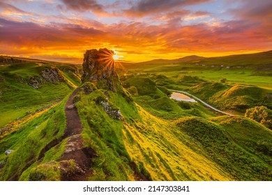 Sunset on the Isle of Skye in Scotland. Sun rays on the mountain hill. Red and orange clouds in the sky. Castle Ewen with paths and meadow in the evening. small lake with road. Sunshine in the valley