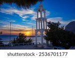 Sunset on Kalymnos, Greece. View of the bell tower and the sea with orange colored sky of the setting sun over the island of Telendos