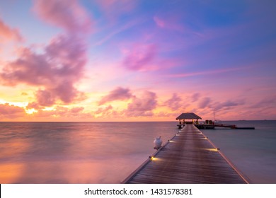 Sunset on Maldives island, luxury water villas resort and wooden pier. Beautiful sky and clouds and beach background for summer vacation holiday and travel concept. Paradise sunset landscape