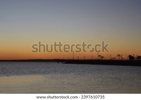 Sunset on the Posadas waterfront. Sunset on the coast of the Paraná River in the city of Posadas. In the background you can see some plants and light headlights.