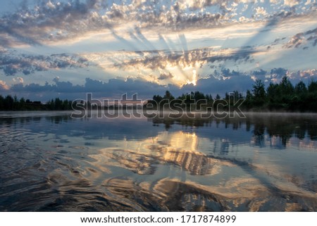 Sunset on the river. The rays of the sun break through the clouds. Reflection in the water.
