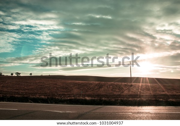 Sunset on a road\
and fields. Dramatic\
landscape