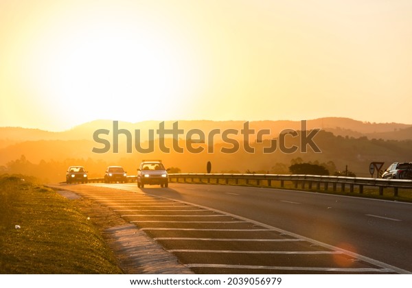 Sunset on the road. Various\
shades of orange in the mountains and cars passing by on the\
highway.\
