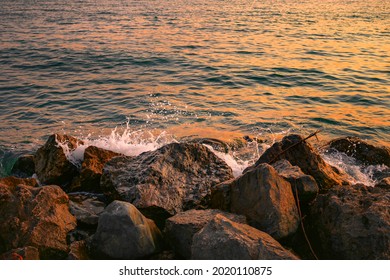 Sunset on a rocky stone beach. Orange sunset on the beach with big stones. Large stones with a beautiful texture against the background of a sea sunset. Evening landscape on the rocky sea shore.