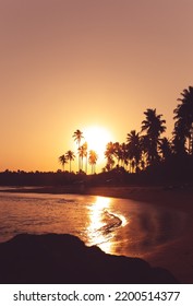 Sunset On A Tropical Island. Silhouette Of Coconut Trees On The Beach With The Sun Going Down In The Background.