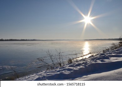 Sunset on the winter river, winter landscape, snow and the sun is shining bright and reflected in the ice water