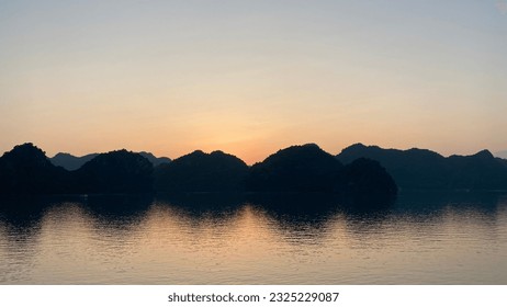Sunset outlining the backlit islands reflected on the water in Ha Long Bay, Vietnam