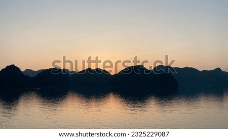Sunset outlining the backlit islands reflected on the water in Ha Long Bay, Vietnam