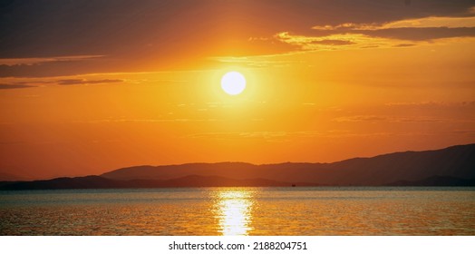 Sunset over Aegean Sea. Greece. Sun falling behind dark land, golden reflections on rippled ocean water. Orange color sky and clouds - Powered by Shutterstock