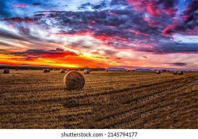 Sunset over an agricultural field with haystacks. Agricultural field with haystacks at sunset. Beautiful sunset over agriculture field. Haystacks on farm field at sunset