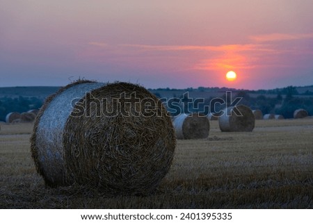 Sunset over an agricultural landscape featuring round bundles of dry hay