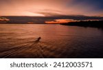 Sunset over the Amazon River in Leticia, Colombia; a boat creates ripples in the tranquil waters, silhouetted against the vibrant sky