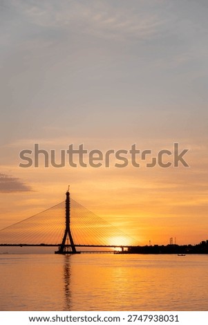 Sunset over cable-stayed bridge silhouette on river at golden hour, dramatic orange sky and water reflection, Danjiang Bridge Taipei Taiwan