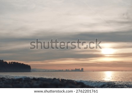 Sunset over a calm ocean with distant skyline, soft clouds and warm reflections on water, tranquil beach foreground and gentle waves at dusk.