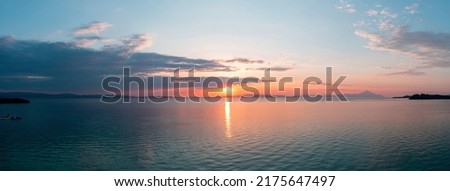 Sunset over calm ocean panoramic view. Dramatic magical sunrise seascape in Aegean Sea, Greece. Sun reflection on the water. Orange and blue color shades.