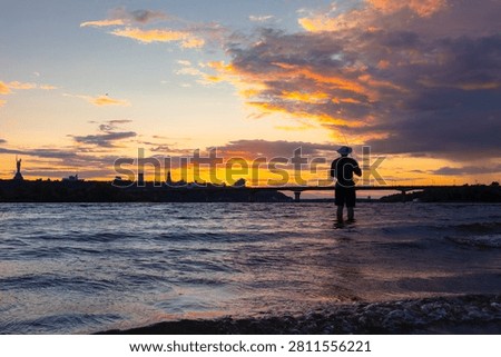 Sunset over the Dnipro River in Kyiv. Ukraine. Silhouette of a fisherman standing in the river water.