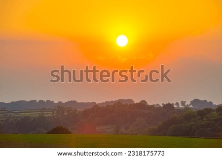 Sunset over fields and trees in a green hilly landscape under a colorful sky in sunlight in spring, Voeren, Limburg, Belgium, June, 2023
