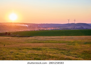 Sunset over green fields with distant wind turbines and clear sky.