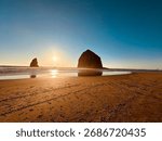 Sunset over Haystack Rock at Cannon Beach, Oregon, with clear skies and sandy shore creating a serene coastal scene.