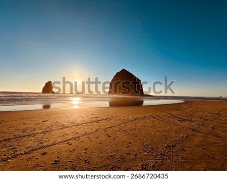 Sunset over Haystack Rock at Cannon Beach, Oregon, with clear skies and sandy shore creating a serene coastal scene.