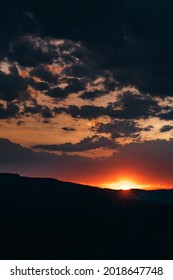 Sunset over the hills with dark clouds. The sun has just reached the peaks and about the rest behind the hill.
