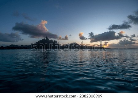Sunset over the island of Bora Bora in Tahiti taken from a deluxe over-water villa at the luxurious St. Regis Resort. Mt. Otemanu silhouetted  against an indigo sky as sunset reflects on vast lagoon.