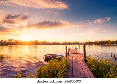 Sunset over the lake in the village. View from a wooden bridge, image in the orange-purple toning - Powered by Shutterstock