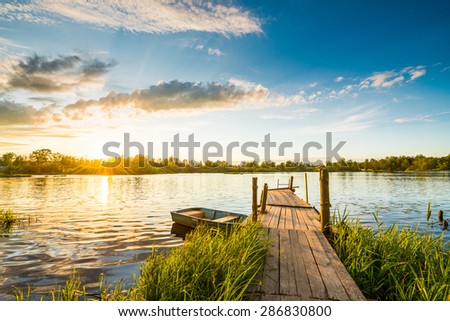 Sunset over the lake in the village. View from a wooden bridge