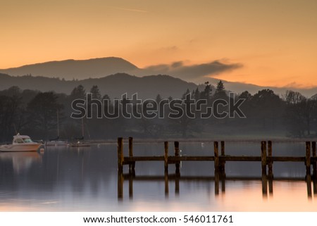 Sunset over Lake Windermere, with woods and mountains in the background. 