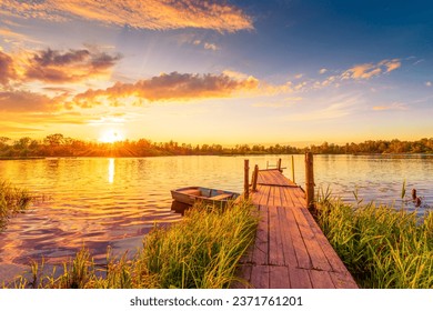Sunset over the lake. Wooden village bridge with a boat. Forest on the horizon. Cloudy sky. Ripples in the water. Reed thickets. View from the bridge. Track and travel. Russia, Europe.