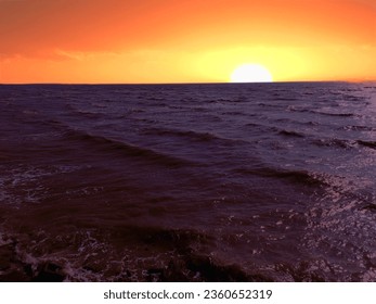a sunset over a large body of water. The sun is low in the sky, and its orange and yellow light is reflected on the water, creating a beautiful and vibrant scene. - Powered by Shutterstock