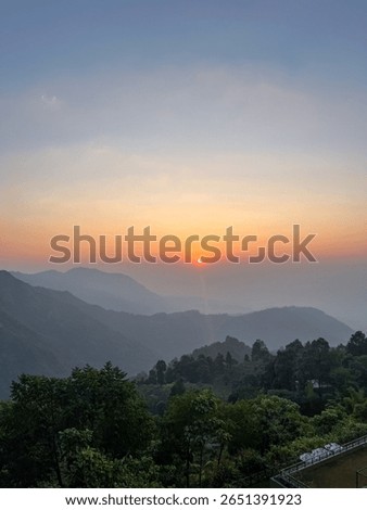 Sunset over the misty mountain range in Makaibari, India’s tea region, with soft fog drifting through lush hills. A serene, golden-hour scene capturing the essence of rural tranquility.