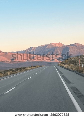 Sunset over a mountain road in eastern Yosemite, USA, with red-hued mountains glowing under vibrant evening skies.
