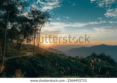 Sunset over the moutain range with flare in Doi Phu Kha National Park, Nan, Thailand. with dirt road and trees in the foreground