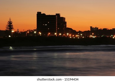 Sunset over the ocean with a pine tree and buildings silhouetted
