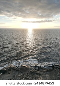 Sunset over ocean with sun path on water and rocky shoreline