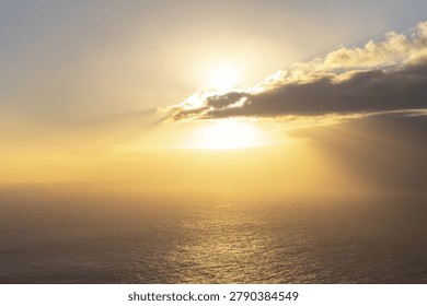 Sunset over the ocean with sun rays breaking through clouds. A golden sunset illuminates the ocean surface as bright sunbeams pierce through a layer of dark clouds over the horizon.