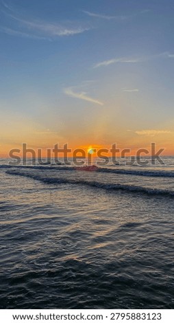 Sunset over the ocean with waves rolling onto the shore. Coastal seascape with golden light reflecting on the water and sandy beach