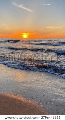 Sunset over the ocean with waves rolling onto the shore. Coastal seascape with golden light reflecting on the water and sandy beach