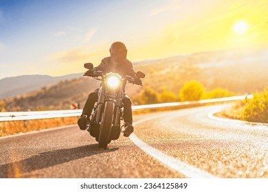 Sunset over an open road and a man with a helmet riding a chopper motorbike