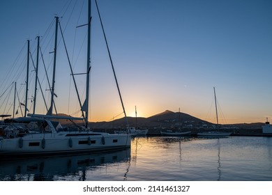 Sunset over Paros Greek island, Cyclades, Greece. Yacht and boat moored at port dock as sun hides behind the hill. Colorful Aegean sea, reflection
