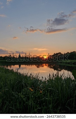 Sunset over the river with the reflection of the sky in the water. A peaceful rural atmosphere. Sunset in a summer village over a lake with a church in the distance.