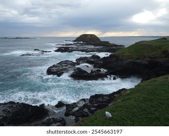 Sunset over a rocky seashore with waves crashing against rocks and distant rain - Powered by Shutterstock