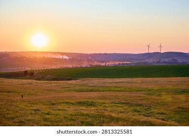 Sunset over rolling fields with wind turbines in the distance.