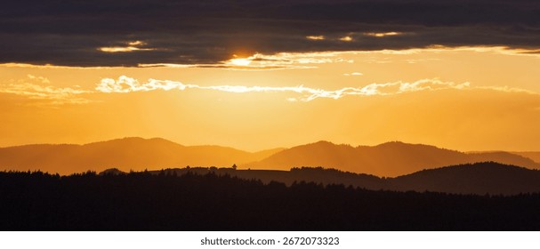Sunset over rolling hills with a dramatic sky. Warm light casts long shadows, creating a serene and scenic landscape.