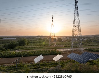 Sunset over rural fields with solar panels power transmission towers and overhead lines