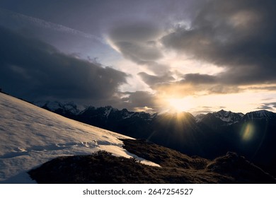 Sunset over the snow-capped Alps with dramatic clouds casting shadows on the mountains